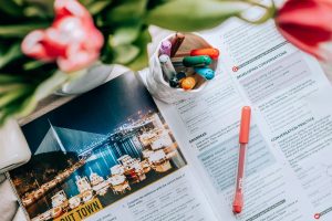 Top view of an open book with pens and markers, surrounded by vibrant flowers, creating a creative workspace vibe.